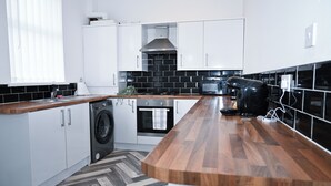 Una cocina moderna con armarios blancos, encimera de madera, lavadora, horno y microondas.