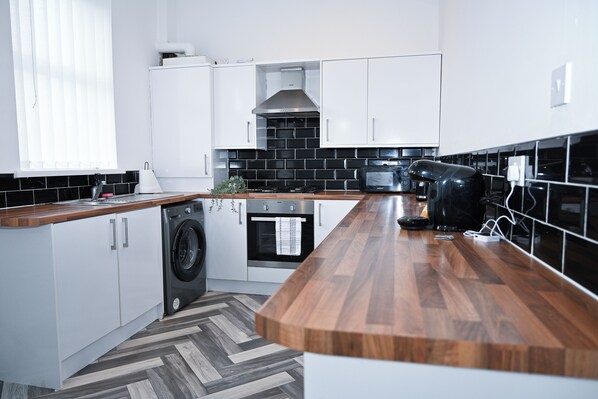 A modern kitchen with white cabinets, a wooden countertop, a washing machine, an oven, and a microwave. - 3BED Home in Sunderland (Sleeps upto 6, Free Parking) 7min to stadium of light (Sunderland)