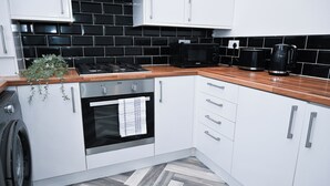 Una cocina moderna con armarios blancos, salpicadero de azulejos negros, encimera de madera, microondas negro y cafetera.