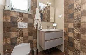 A bathroom with patterned tiles, a toilet, a sink with a mirror, and a towel hanging on the wall. - Stunning home in Banj (Banj)
