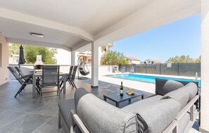 A covered outdoor area with a pool, lounge chairs, and a table with a bottle and glasses. - Stunning home in Banj (Banj)