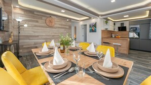 A dining area with a wooden table set for four, yellow chairs, and a kitchen in the background.