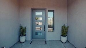 Una entrada moderna amb una porta grisa, plantes en testos i una petita finestra.