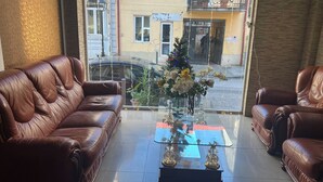 A living room with two brown leather sofas, a glass coffee table with decorative items, and a view of a street with a parked car and a building with balconies. - hotel golden star (Batumi)