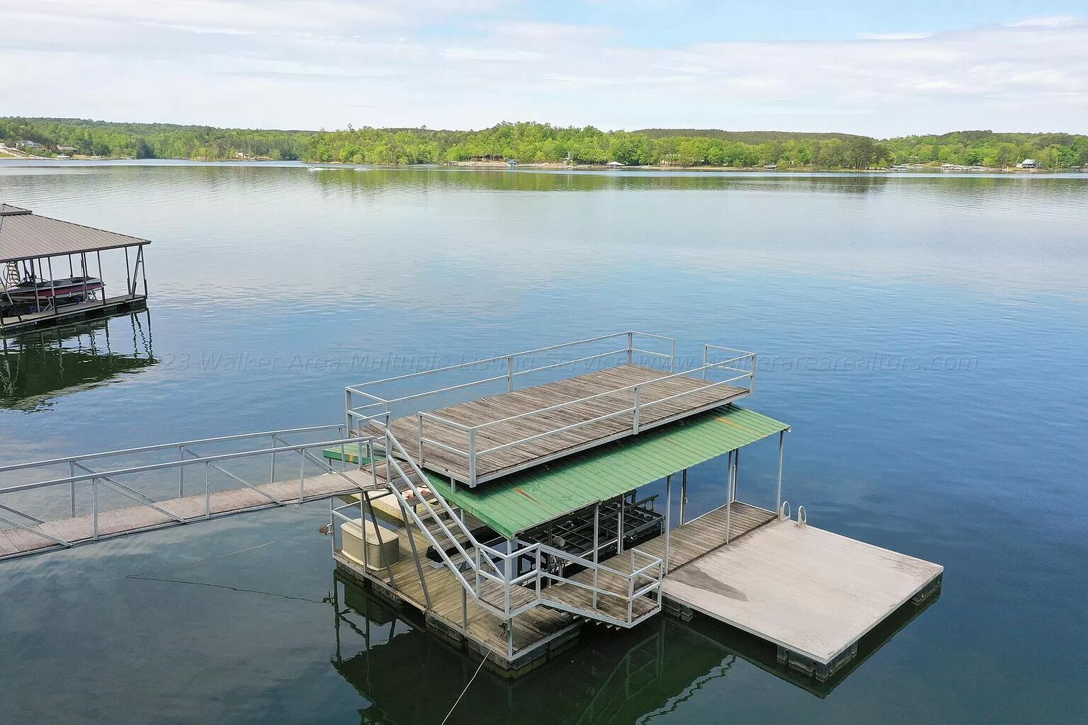 A dock with a green roof and a metal railing, extending into calm water.