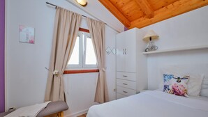 Ein Schlafzimmer mit einem Bett, einem Nachttisch, einem Fenster mit Vorhängen, einer Holzbalkendecke und einem Wandregal mit einer Lampe.