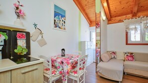 Ein gemütliches Wohnzimmer mit Holzboden, ein Essbereich mit einer Tischdecke mit Blumenmuster und eine Couch mit floralen Kissen.