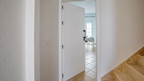 Ein Flur mit einer weißen Tür, die in einen Raum mit gefliestem Boden und einem Fenster führt.