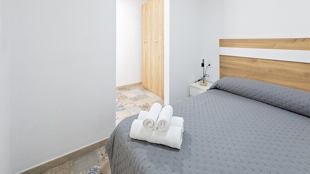 Ein Schlafzimmer mit Bett, Nachttisch, Holzschrank und einem durchgegangenen Tür sichtbar erkennbaren Badezimmer.