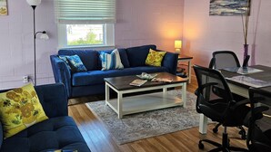 Una sala de estar con un sofá azul, una mesa de centro, un escritorio con una silla y una lámpara.