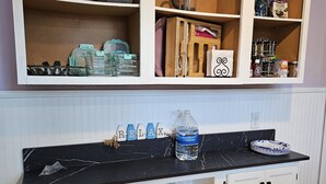 Una cocina con armarios blancos, encimera negra y varios utensilios de cocina, como dispensador de agua, ollas y frascos.
