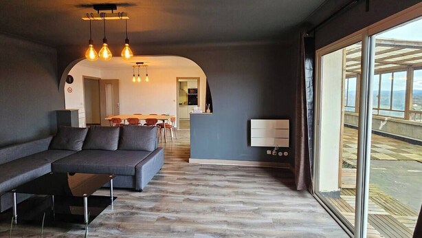 A modern living room with a sofa, a coffee table, and a dining area with a table and chairs. There is a large window providing a view of the outdoors. - 3-bedroom 110m² apartment with terrace, view (Thiers)