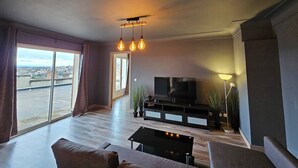 A modern living room with a large flat-screen TV, a coffee table, and a sofa. There is a large window providing a view of the cityscape. - 3-bedroom 110m² apartment with terrace, view (Thiers)