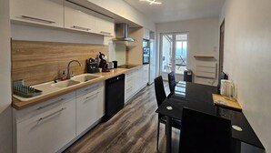 A modern kitchen with white cabinets, a wooden countertop, and a dining area with a black table and chairs. - 3-bedroom 110m² apartment with terrace, view (Thiers)