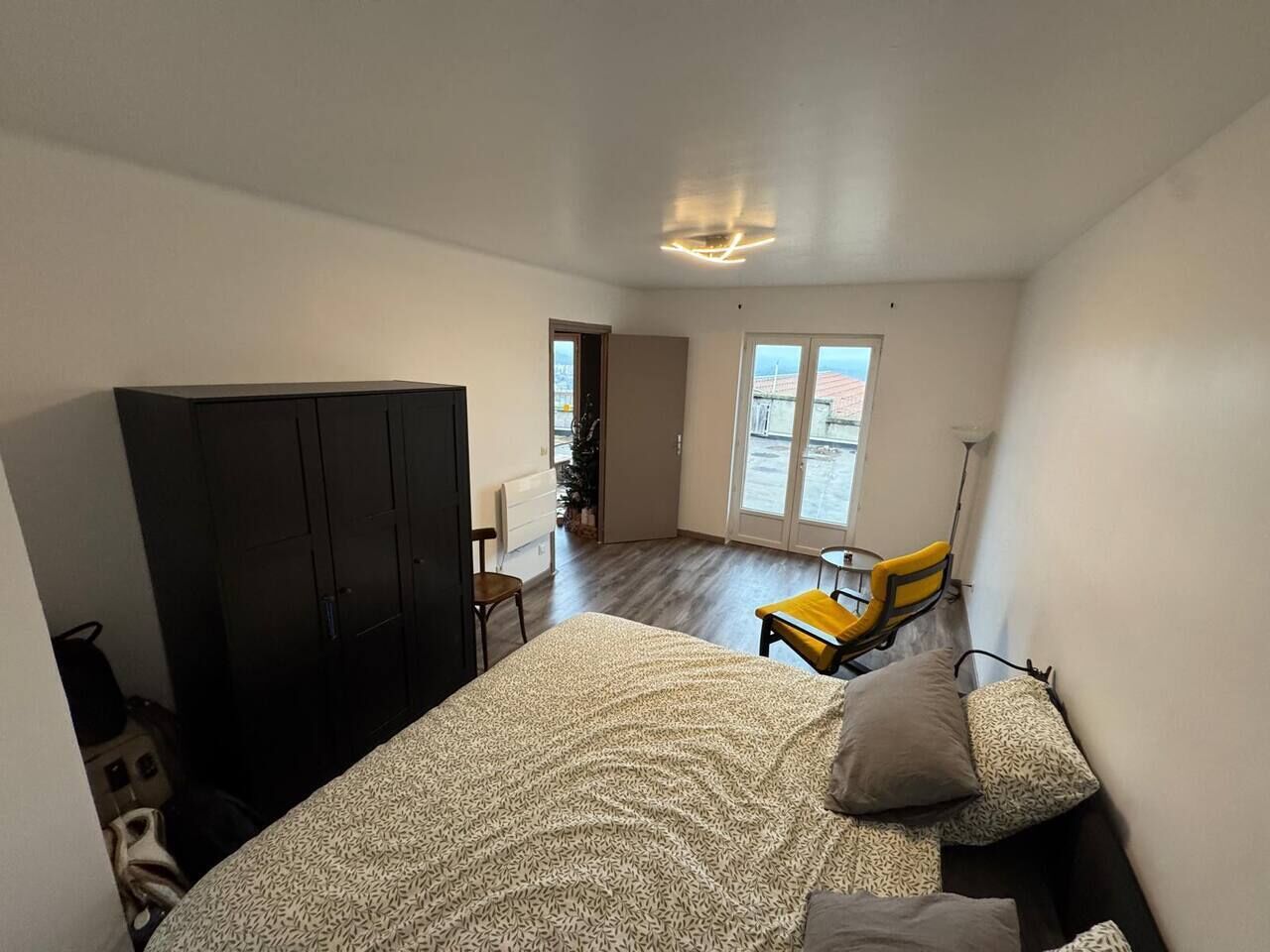 Un dormitorio con cama, armario, silla y una mesita.