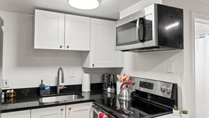 A modern kitchen with white cabinets, a black countertop, stainless steel appliances, and a kettle. - Cozy 1 Bed, 1 Bath - Near Downtown and U of U. (Salt Lake City)
