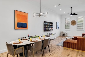 A modern dining area with a long table, chairs, a chandelier, and a television mounted on the wall.