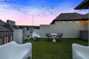 Una terraza en la azotea con césped artificial, una mesa blanca y sillas negras.
