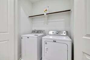 Une buanderie avec deux machines à laver à chargement frontal, toutes deux de couleur blanche, et une étagère placée au-dessus.