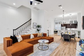 A modern living room with a sectional sofa, a dining area, and a kitchen.