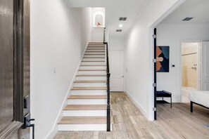 A staircase with wooden steps and black balusters, leading to a room with a bed and a shower area.
