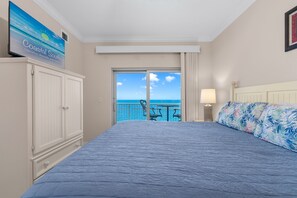 A bedroom with a large bed, a view of the ocean, a balcony with chairs, and a sign for Coastal South Vacation Rentals. - Luxury Corner Condo 3 Pools, Lazy River. Amazing Views. Fall Fun (Gulf Shores)