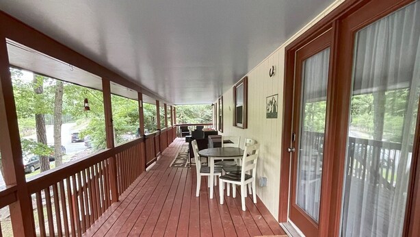 A covered porch with a wooden deck, a dining table with chairs, and a sofa with a cushion. - Relax at Skylark's Nest (McGaheysville)