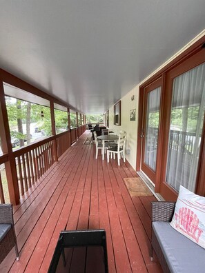 Eine überdachte Veranda mit Holzterrasse, einem Esstisch mit Stühlen und einer Couch mit Kissen.