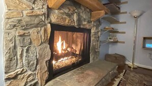 A stone fireplace with a fire, a wooden shelf above it, and a patterned rug on the floor. - Relax at Skylark's Nest (McGaheysville)