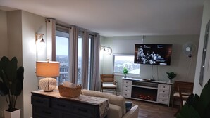 A modern living room with a sofa, a TV, a fireplace, and large windows.