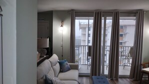 A living room with a sofa, a bench, a lamp, and a view of a balcony with outdoor furniture.