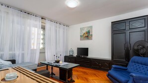 Een woonkamer met een bank, een televisie, een kast en een schilderij aan de muur.