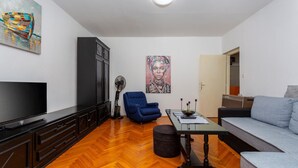 Een woonkamer met een televisie, een blauwe fauteuil, een bank, een tafel en kunstwerken aan de muren.