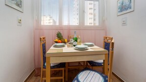 Een eettafel gedekt voor vier personen, met stoelen, een raam met dunne gordijnen en kunstwerken aan de wanden.