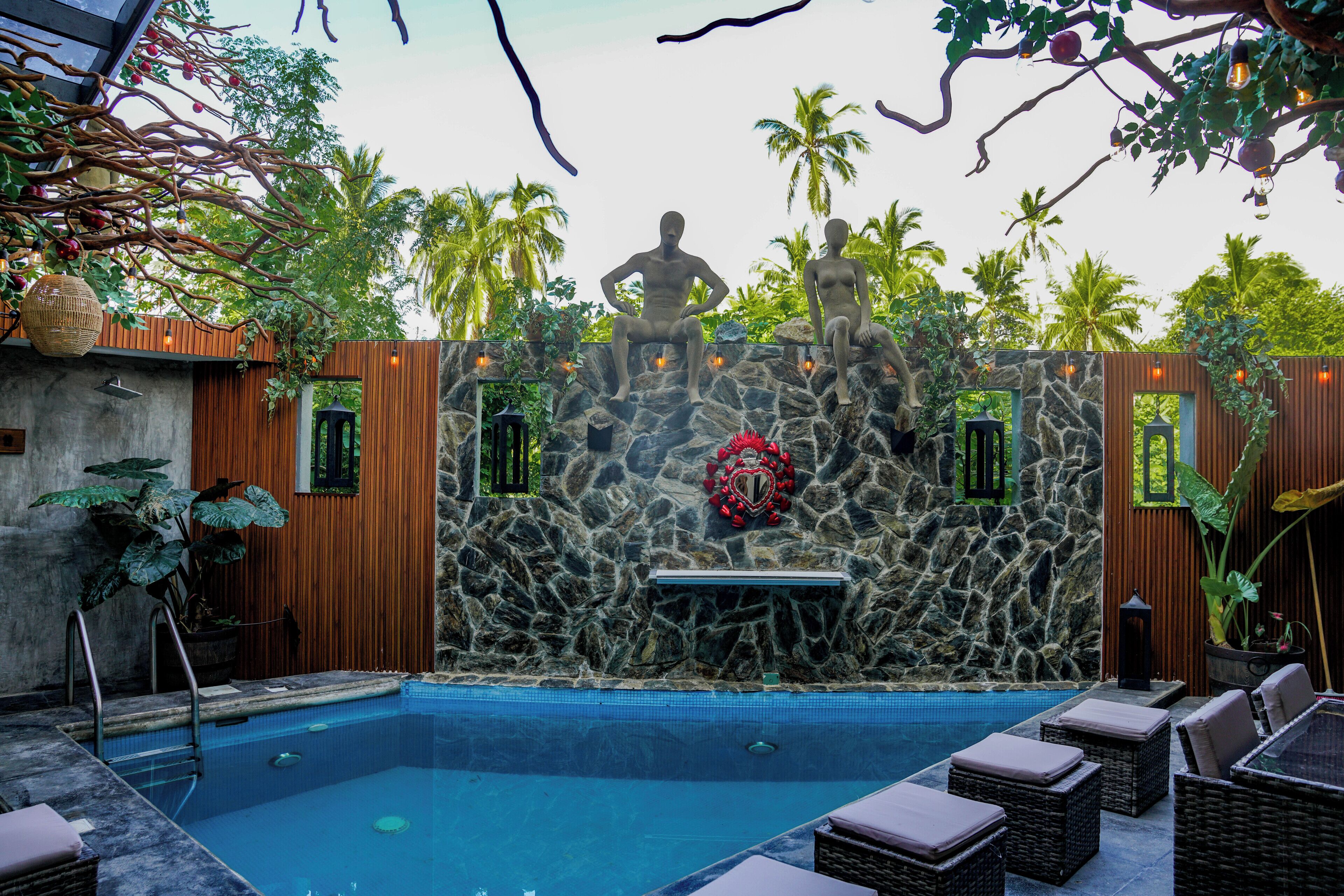 Un área de piscina con muros de piedra, una estatua y sillones de descanso.