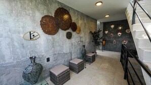Een modern interieur met een betonmuur, decoratieve metalen kunst, een glazen vaas, rieten poefs en een trap met metalen leuning.