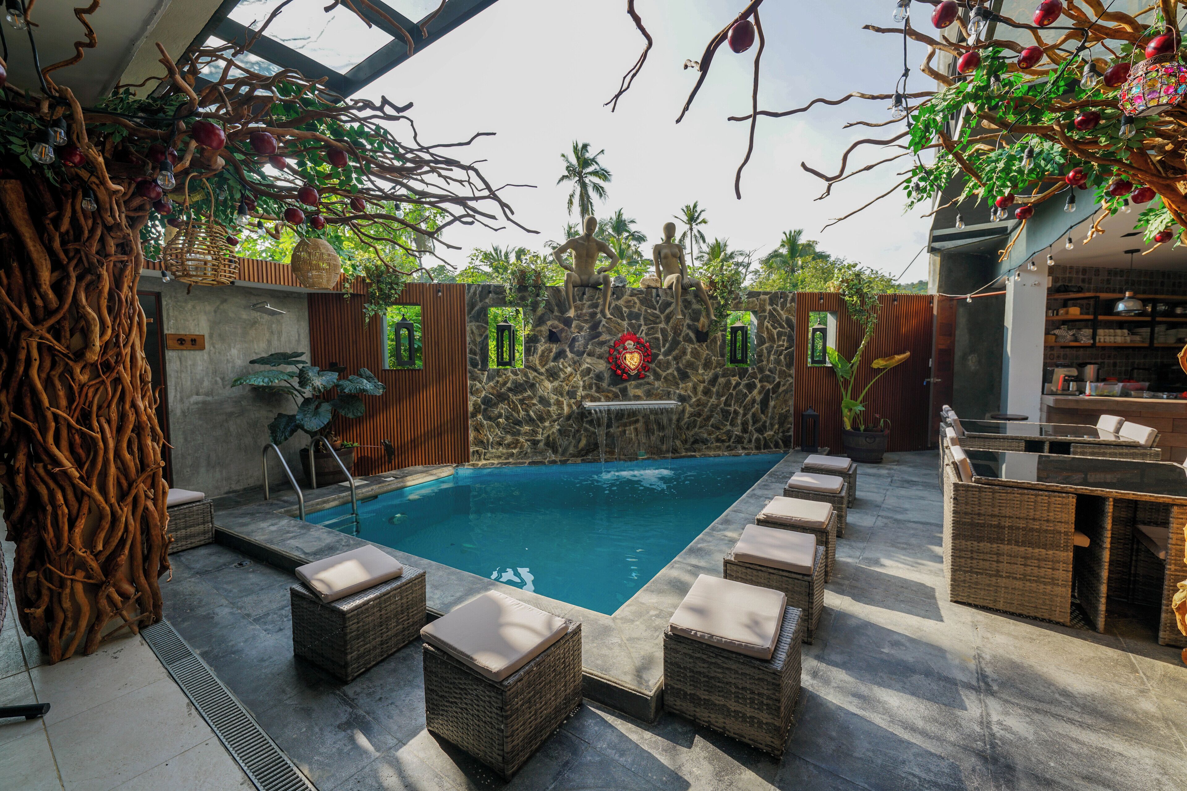 A pool area with wicker furniture, a stone wall, and a waterfall feature.