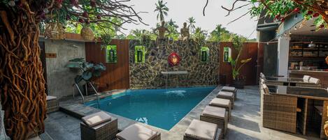 A pool area with wicker furniture, a stone wall, and a waterfall feature.