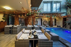 Un espace piscine intérieur aménagé avec des meubles en osier et un coin repas.