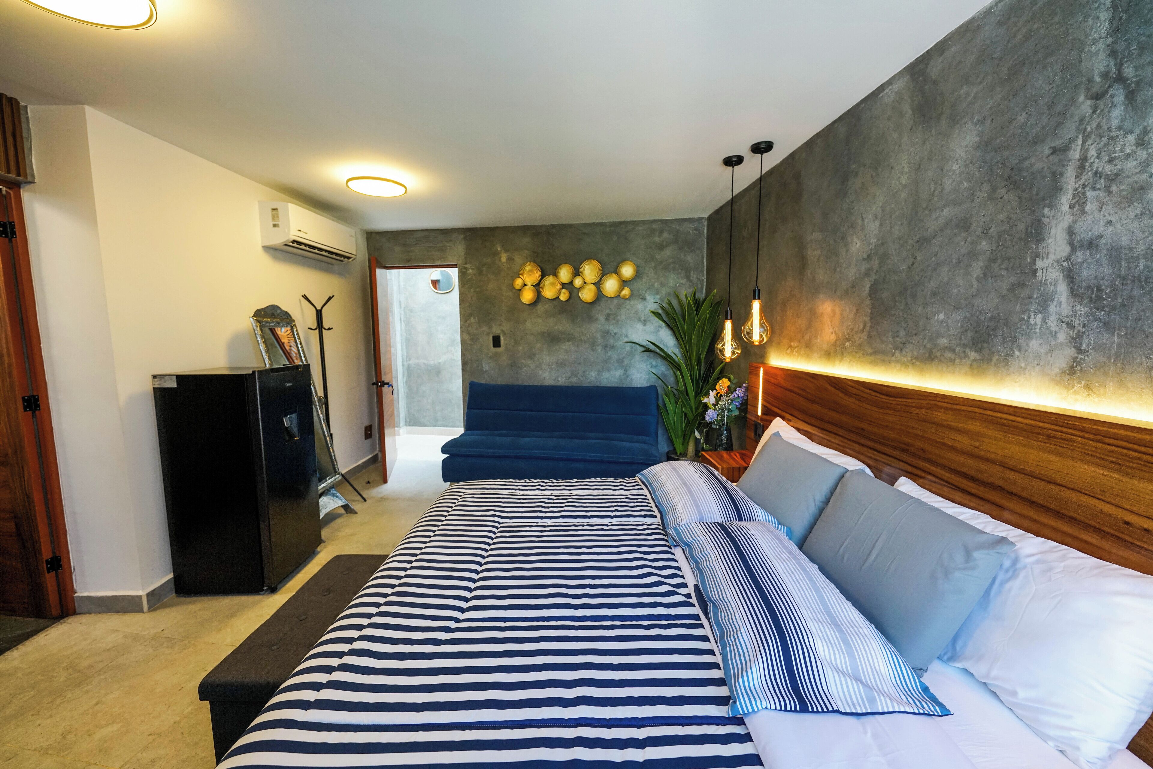 Un dormitorio moderno con una cama grande, un cabecero azul oscuro y un aire acondicionado instalado en la pared.