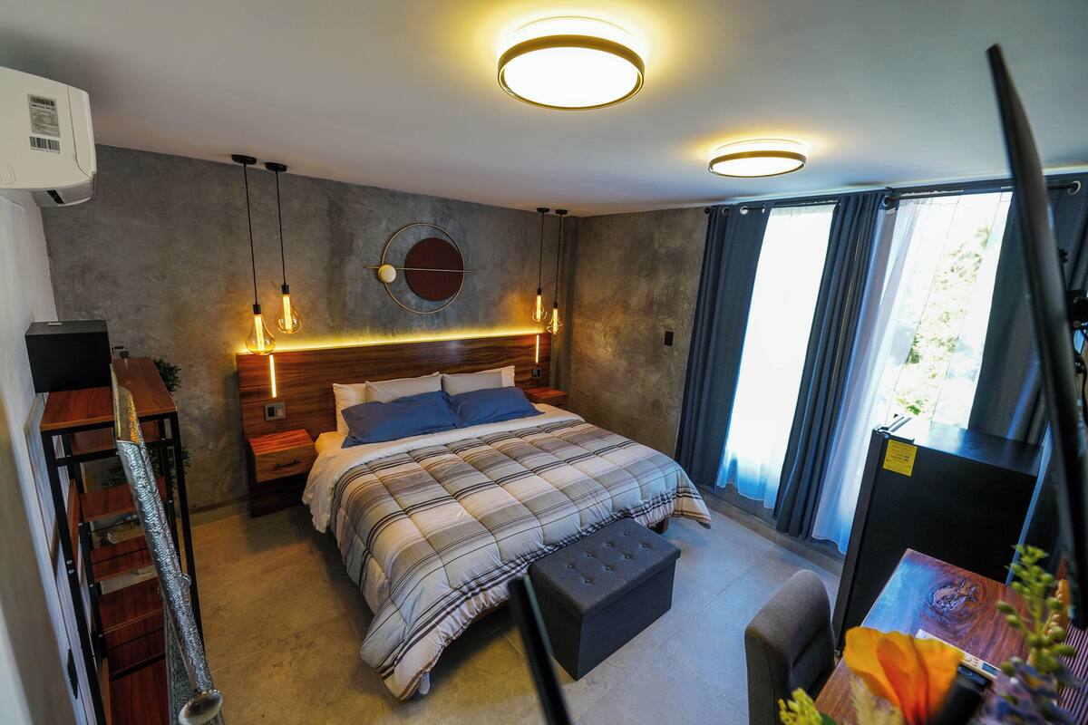 Une chambre moderne avec un grand lit, des tables de chevet, une horloge murale ronde et une vue sur l’extérieur par la fenêtre.