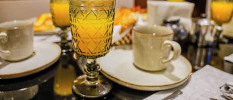 A breakfast setting with a table set for two, including plates, cups, and a glass with a yellow beverage.