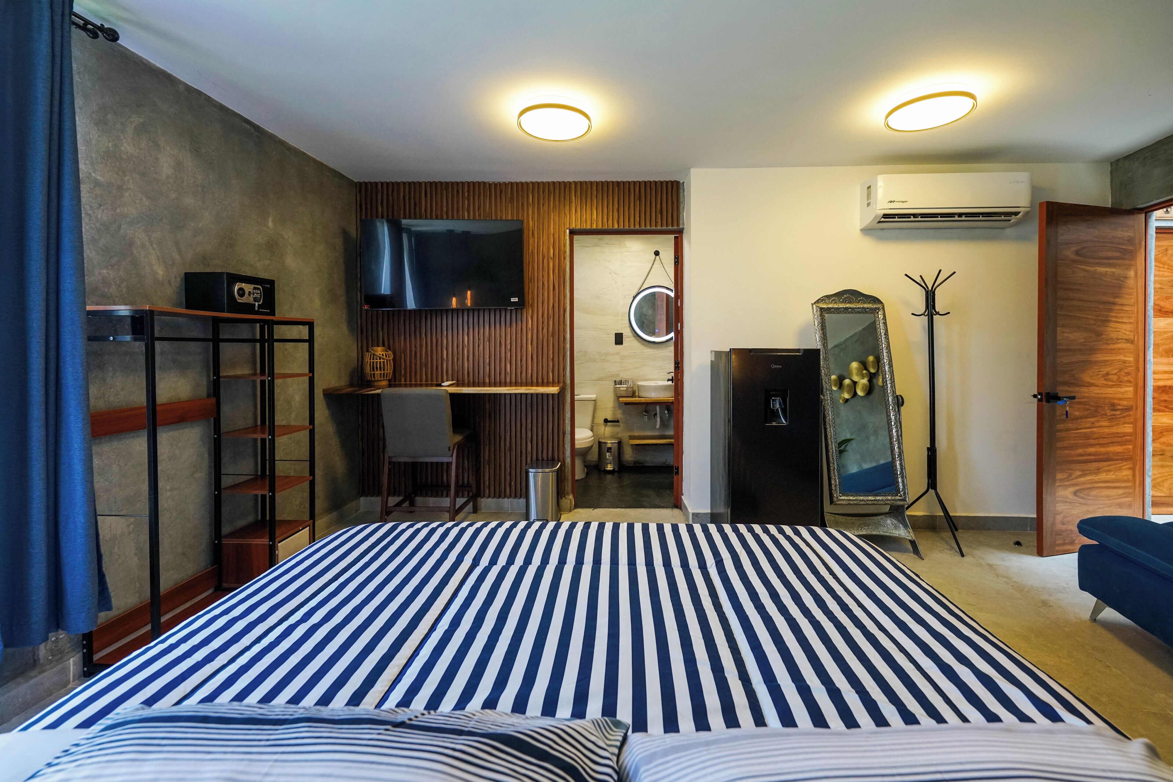 Une chambre à coucher avec un grand lit, un téléviseur fixé au mur, un bureau avec une chaise et un miroir.