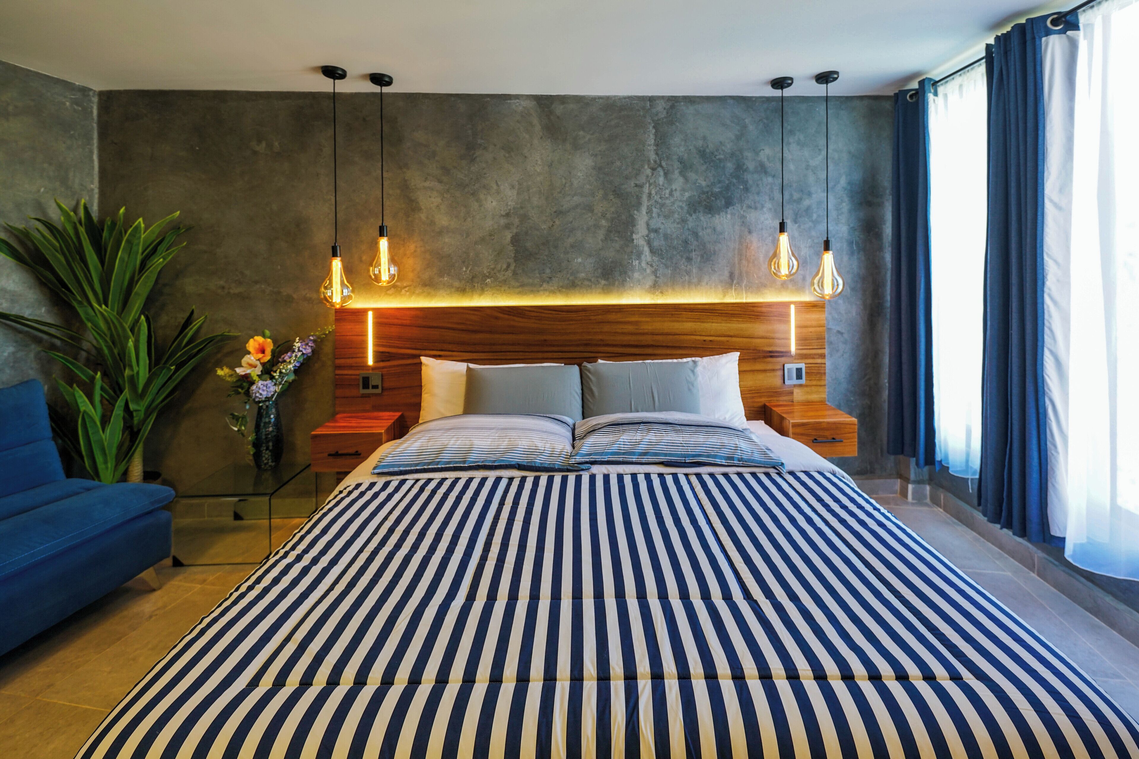 A modern bedroom with a large bed, wooden headboard, bedside tables, and hanging light fixtures.