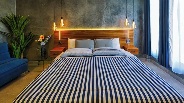 A modern bedroom with a large bed, wooden headboard, bedside tables, and hanging light fixtures. - Hotel El Edén  (San Pedro Pochutla)