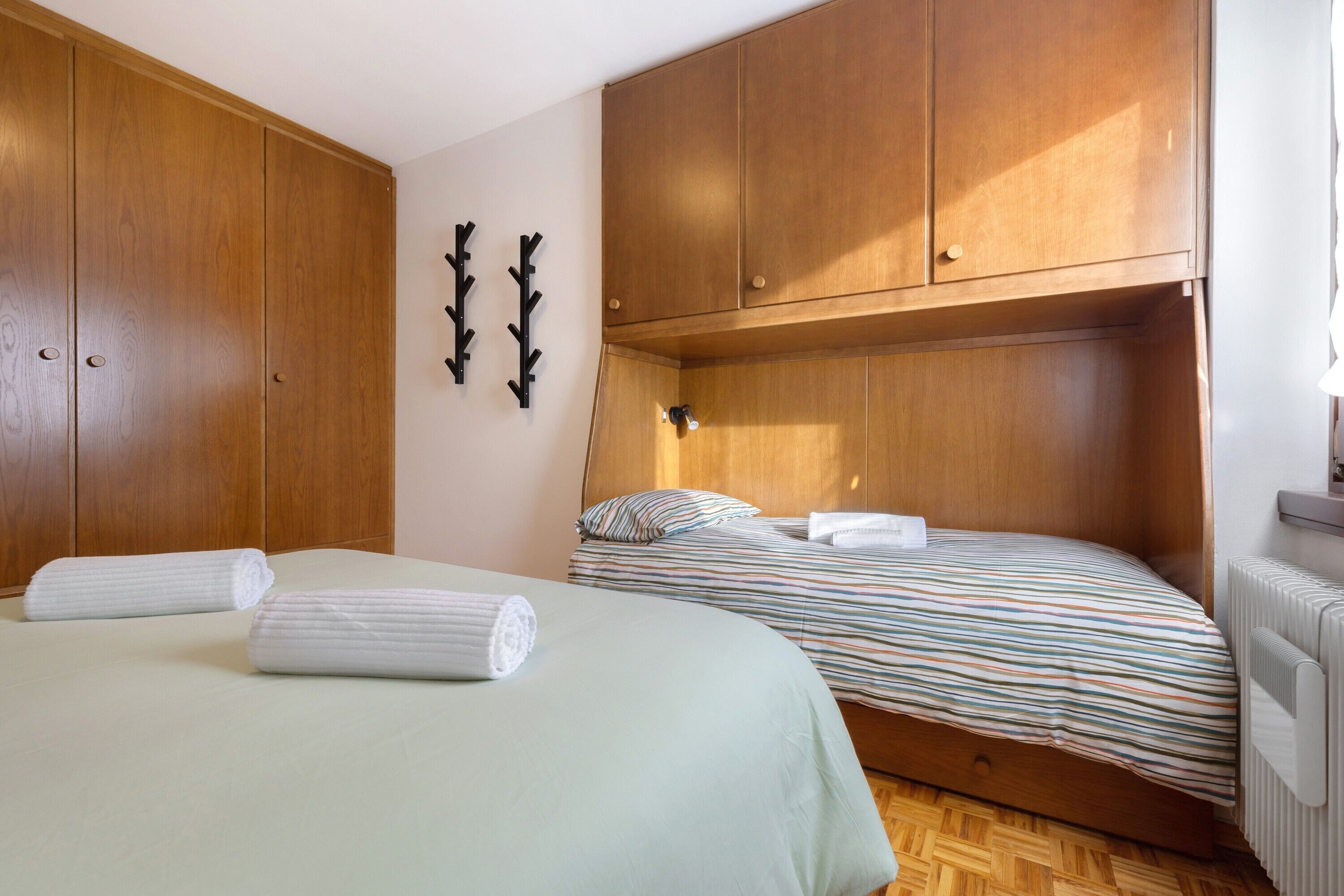 Ein Schlafzimmer mit zwei Betten, Holzschränken, einem Heizkörper und Wandhaken.