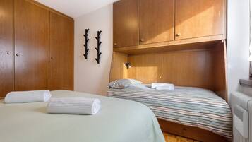 Ein Schlafzimmer mit zwei Betten, Holzschränken, einem Heizkörper und Wandhaken.