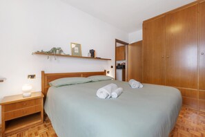 A bedroom with a bed, wooden wardrobe, nightstand, and a shelf with a plant. - La Finestra sui Monti – Apartment with Terrace and Dolomiti di Brenta View (Breguzzo)