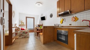 A kitchen with wooden cabinets, a built-in oven, a TV mounted on the wall, and a dining area with a table and chairs.