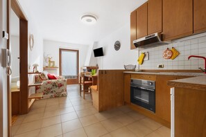A kitchen with wooden cabinets, a built-in oven, a TV mounted on the wall, and a dining area with a table and chairs. - La Finestra sui Monti – Apartment with Terrace and Dolomiti di Brenta View (Breguzzo)
